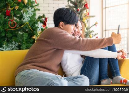 Young asian adult teenager coupletake selfie photographing for celebrateing christmas holiday together in living room with christmas tree decoration.