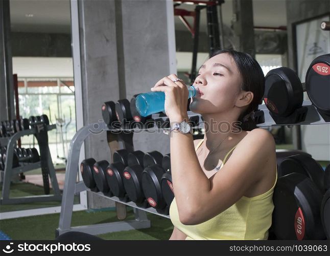 Young Asian athlete woman drinking sport drink after exercise in fitness gym, healthy lifestyle concepts