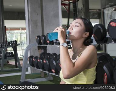 Young Asian athlete woman drinking sport drink after exercise in fitness gym, healthy lifestyle concepts