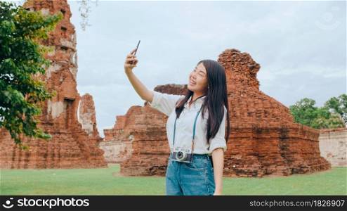 Young Asian backpacker blogger woman casual take selfie video call on mobile phone sharing live online for audience travel together at pagoda old city, Lifestyle tourist travel holiday concept.