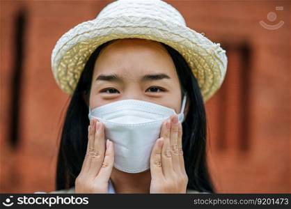 Young asian backpacker female wearing hat and protection mask while traveling in historic site, she use camera take a photo with happy