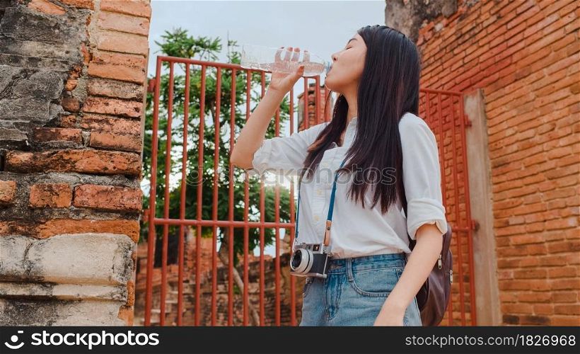 Young Asian backpacker woman blogger tourist with camera feel tired stand in front of pagoda take a rest and drink water in plastic bottle at old town , Lifestyle tourist travel holiday concept.