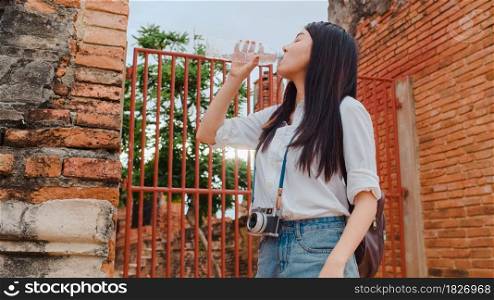 Young Asian backpacker woman blogger tourist with camera feel tired stand in front of pagoda take a rest and drink water in plastic bottle at old town , Lifestyle tourist travel holiday concept.