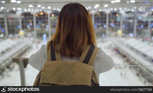 Young Asian backpacker woman looking around in terminal hall while waiting her flight at the departure gate in international airport. Lifestyle backpack tourist travel holiday concept.