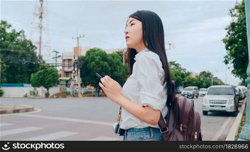 Young Asian backpacker woman tourist with camera stand in front of cross walk street look at mobile phone search navigation application for the location, Lifestyle tourist travel holiday concept.
