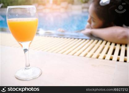 Young asian Beautiful woman relaxing in swimming pool with orange mocktail in classic glass