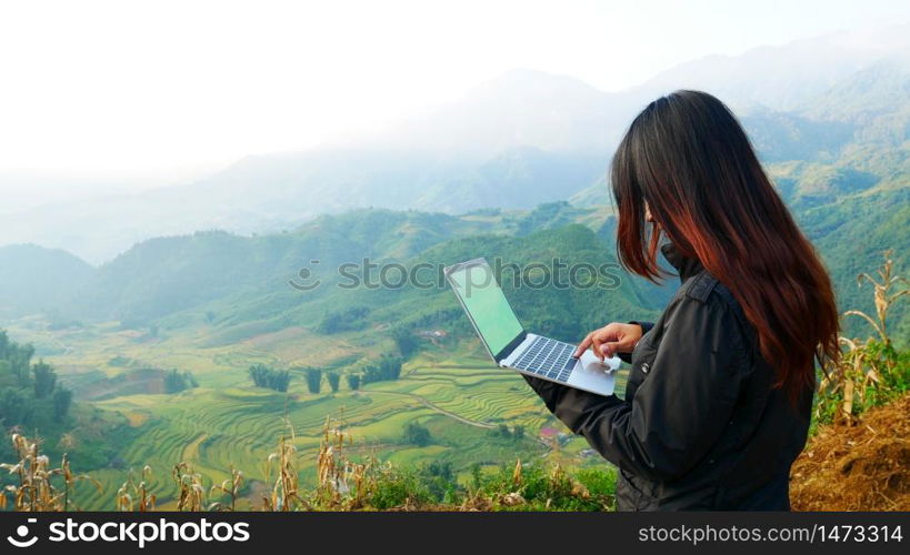 Young Asian beautiful woman with smiling face working outdoor in a public park. Working on laptop outdoors. Cropped image of female working on laptop while sitting in a park.