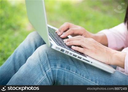 Young Asian beautiful woman with smiling face working outdoor in a public park. Working on laptop outdoors. Cropped image of female working on laptop while sitting in a park.