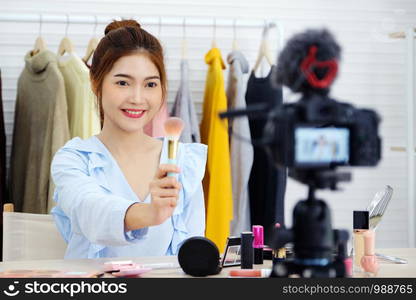 Young asian beauty blogger holding brush while recording video tutorail make up with beauty products at home, beauty and fashion lifestlye blog