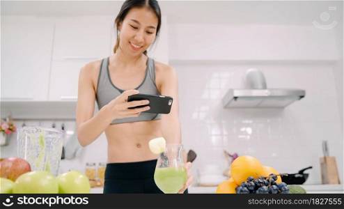 Young Asian blogger woman using smartphone photo post in social media in the kitchen, female in sport clothing making salad at home. Lifestyle women relax at home concept.