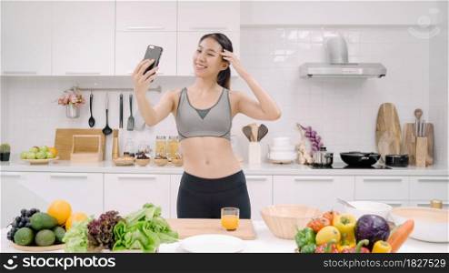 Young Asian blogger woman using smartphone selfie herself in the kitchen, female in sport clothing cooking at home. Lifestyle women relax at home concept.