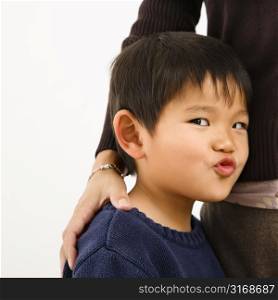 Young Asian boy making funny face standing next to mother.