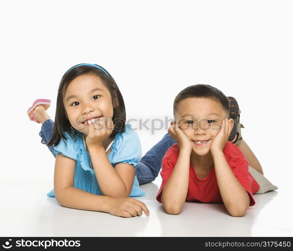 Young Asian brother and sister lying on floor with head on hands.