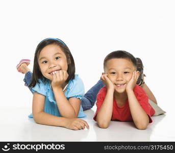 Young Asian brother and sister lying on floor with head on hands.