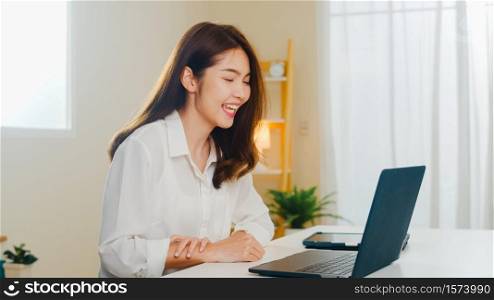 Young Asian business female using laptop video call talking with couple while working from home at living room. Self-isolation, social distancing, quarantine for coronavirus in next normal concept.