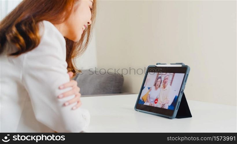 Young Asian business female using tablet video call talking with family dad and mom while working from home at living room. Self-isolation, social distancing, quarantine for coronavirus prevention.