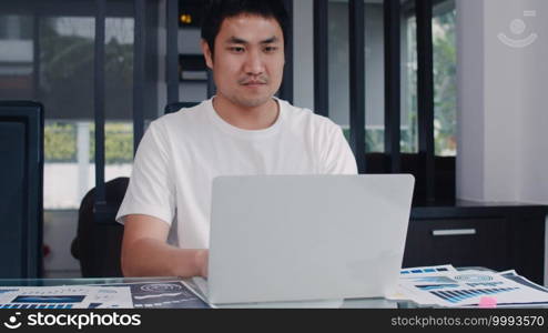 Young Asian business man records of income and expenses at home. male worried, serious, stress while using laptop record budget, tax, financial document working in living room at home concept.