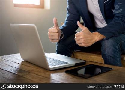 young asian business man showing thumb up while sitting in a cafe and working with laptop.