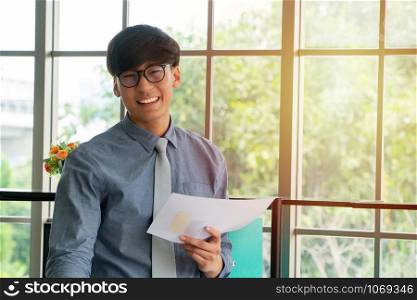 Young Asian businessman excited happy and celebrating success in the workplace after see finalizing the annual sales report. Concept of new entrepreneur successful