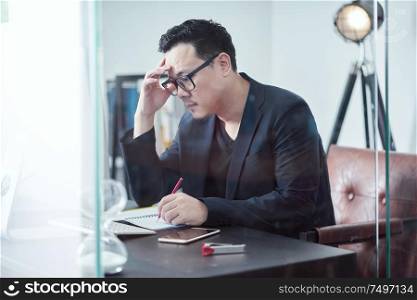 Young Asian businessman feeling exhausted and tired while sitting at his working place .