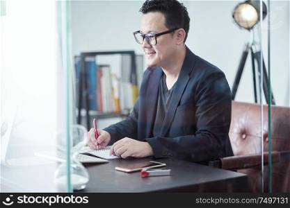Young Asian businessman feeling happy while sitting at his working place .