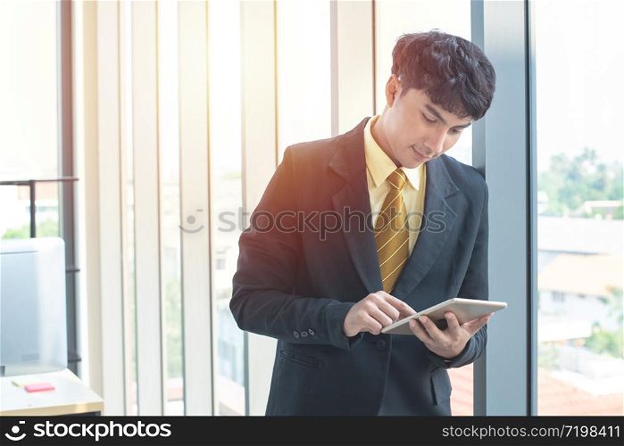 Young asian businessman sitting and working on desk and using digital tablet connecting internet and documents at office, employee or company ceo using online apps software at workplace