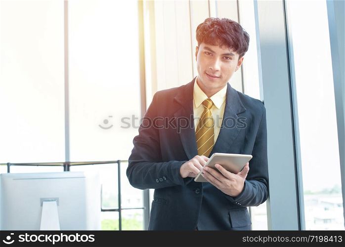 Young asian businessman sitting and working on desk and using digital tablet connecting internet and documents at office, employee or company ceo using online apps software at workplace