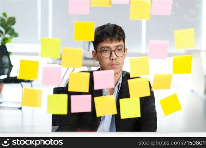 Young asian businessman thinking while reading sticky notes at office, business brainstroming creative planing ideas to success in business concept