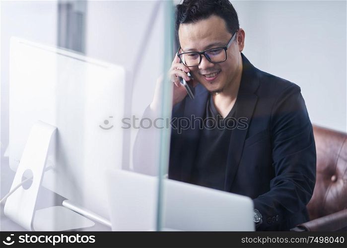 Young asian businessman using handphone and computer working