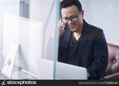 Young asian businessman using handphone and computer working
