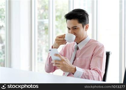 Young asian businessman using smart phone and drinking coffee at office, office life and business concept