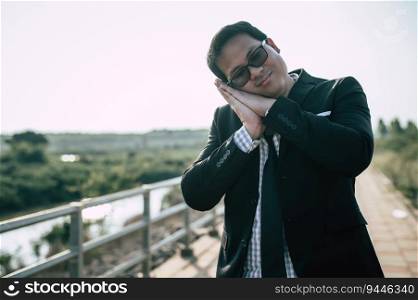Young Asian Businessman wearing suit with tie and glasses close his eyes with tired and sleeping for relaxing at outdoors
