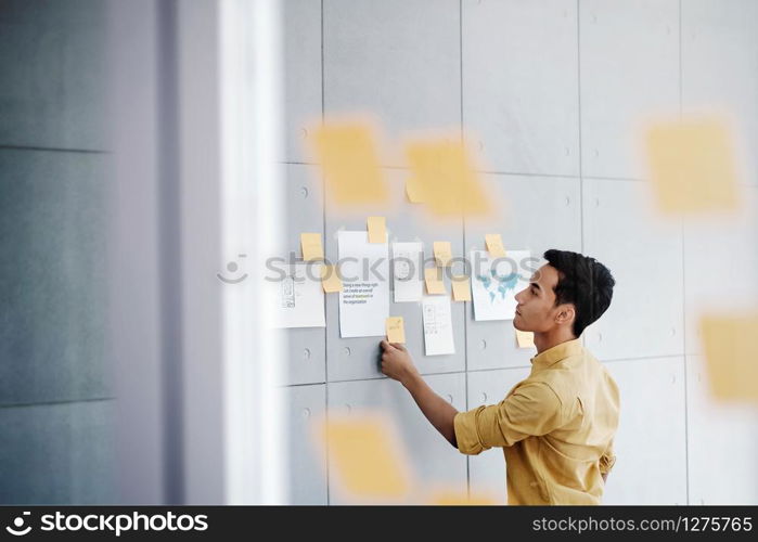 Young Asian Businessman Working in Office Meeting Room. Concentrate on Document Note at the Wall. Man Analyzing Data Plans and Project