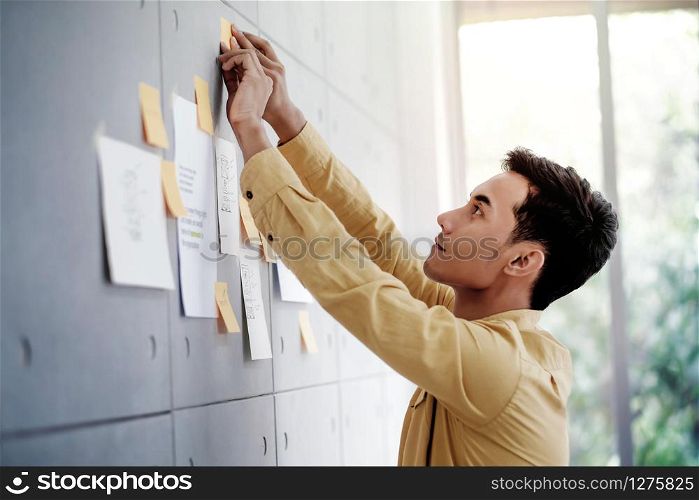 Young Asian Businessman Working in Office Meeting Room. Concentrate on Document Note at the Wall. Man Analyzing Data Plans and Project