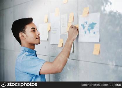 Young Asian Businessman Working in Office Meeting Room. Man Analyzing Data Plans and Project. Concentrate on Document Note on Board