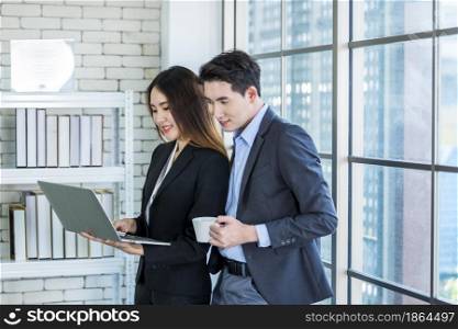 Young Asian businesswoman and businessman partners while working together with laptop computer and business man holding a tablet in office background,Working couple