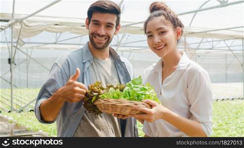 Young Asian businesswoman farmer product selling good quality plant and vegetable with hispanic man buyer looking at camera at organic farm in greenhouse garden, Farm innovation technology concept.