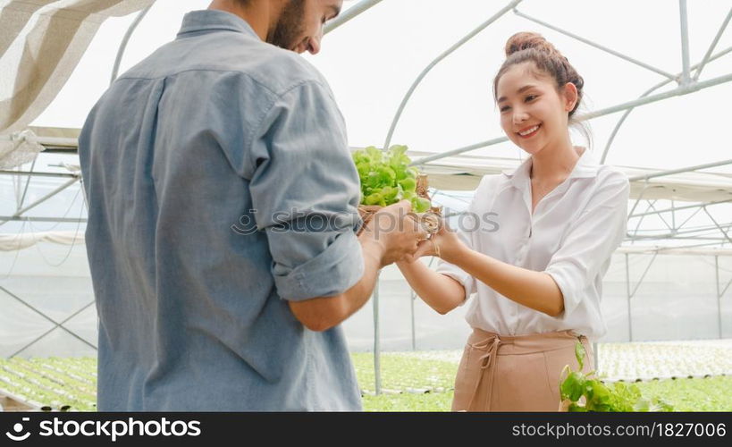 Young Asian businesswoman farmer show product selling good quality plant and vegetable to hispanic man buyer at organic farm in greenhouse garden, New innovation technology the cultivation concept.