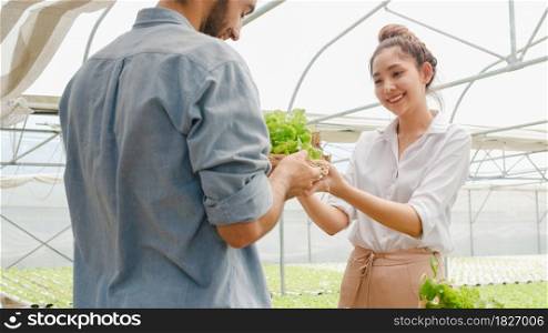 Young Asian businesswoman farmer show product selling good quality plant and vegetable to hispanic man buyer at organic farm in greenhouse garden, New innovation technology the cultivation concept.