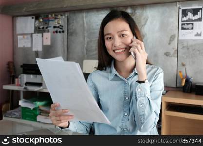 Young asian businesswoman talking phone and holding papers at office table, business casual lifestyle