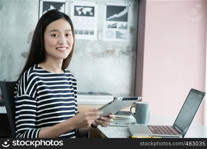 Young asian businesswoman using tablet with smiling face, positive emotion, at office, casual office life concept