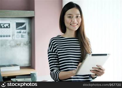 Young asian businesswoman using tablet with smiling face, positive emotion, at office, casual office life concept