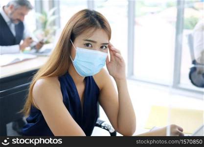 Young Asian businesswoman wearing mask preventing for Covid 19 virus and have a headache and Feel sickness in office. Social distance and new normal lifestyle concept