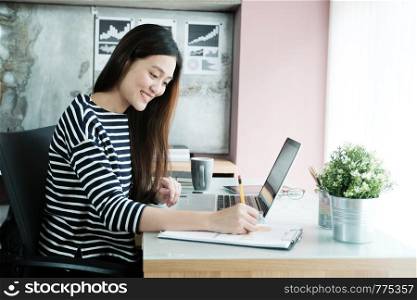 Young asian businesswoman working on paper and laptop computer at office with happy emotion, working at home, office casual lifestyle concept