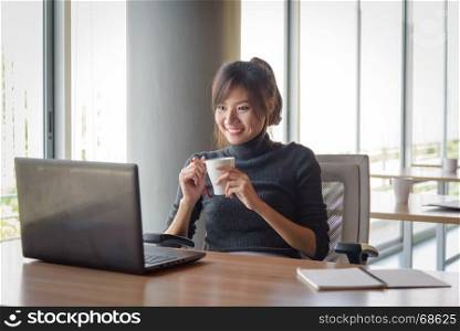 young asian businesswoman working while holding white cup coffee in the office
