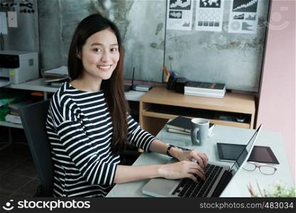 Young asian businesswoman working with laptop with smiling face at office desk, positive emotion, office life concept