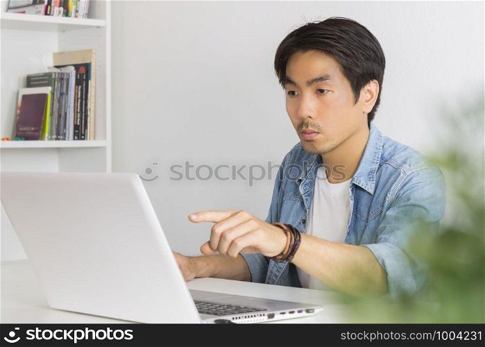 Young Asian Casual Businessman Pointing Laptop Monitor at Workplace in Home Office. Casual business or informal business in home office