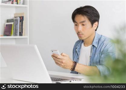 Young Asian Casual Businessman Send Messages to Colleague at Workplace in Home Office. Casual business or informal business in home office