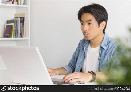 Young Asian Casual Businessman Working with Laptop at Workplace in Home Office. Casual business or informal business in home office