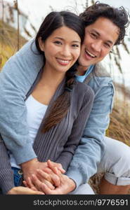 Young Asian Chinese man and woman, boy girl, couple sitting in tall grass smiling with perfect teeth on a romantic date outside